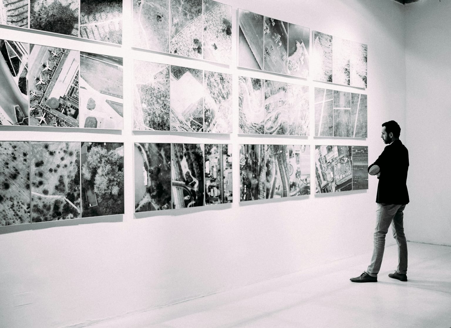 Ein monochromes Raster aus fast identischen Luftaufnahmen in einer Galerie — austauschbare Einheiten, die zu einer einzigen verschwimmen.